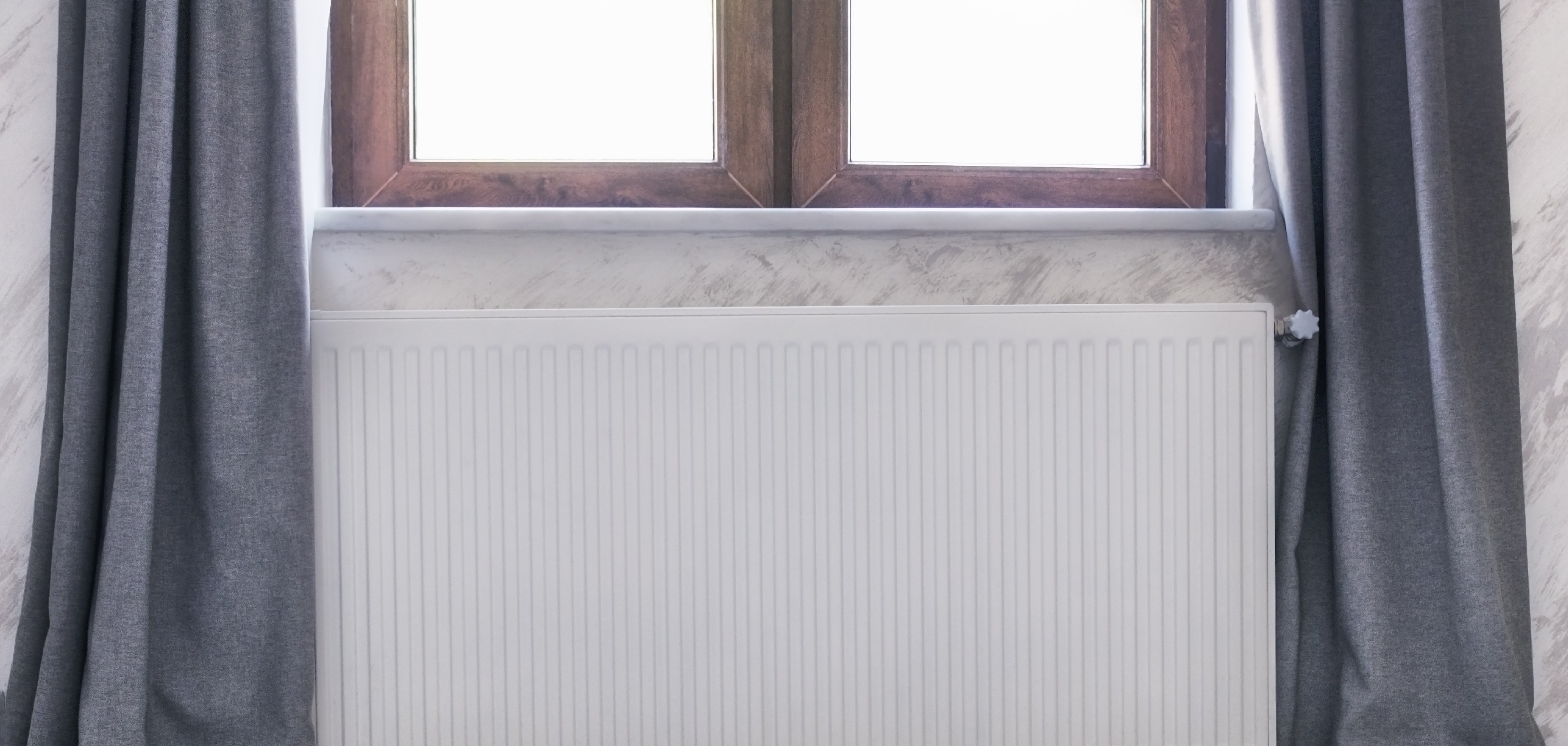 Heizkörper unter dem Fenster mit Holzrahmen und Vorhängen.
