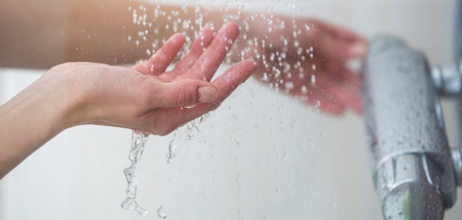 Weibliche Hände testen die Temperatur des Wassers in der Dusch