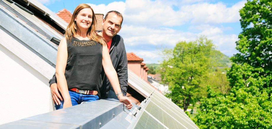 Auf dem Foto ist ein Paar mittleren Alters zu sehen, das sich über seine Photovoltaikanlage auf dem Hausdach freut.