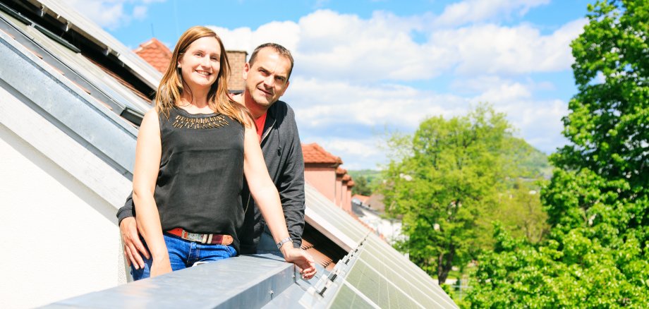 Auf dem Foto ist ein Paar mittleren Alters zu sehen, das sich über seine Photovoltaikanlage auf dem Hausdach freut.