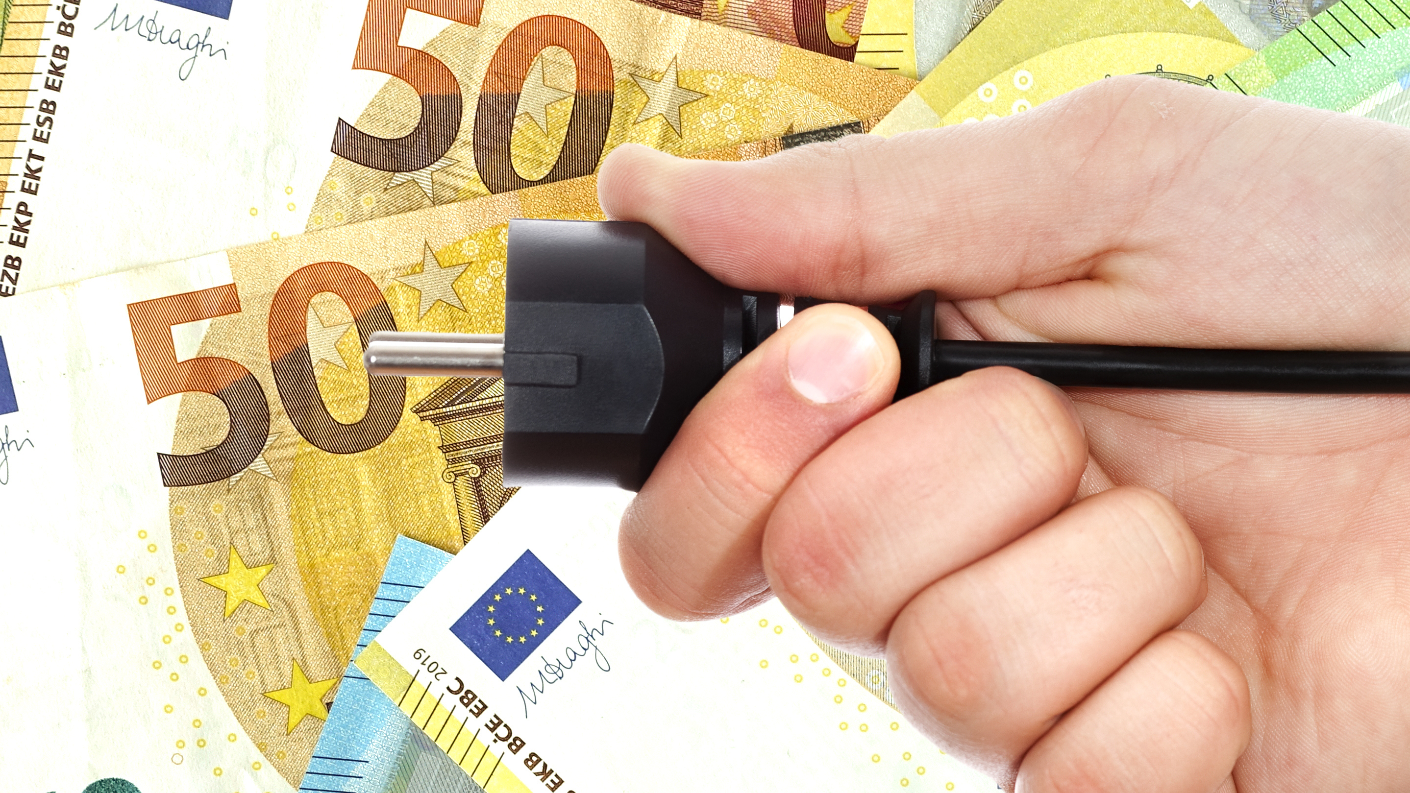 Männliche Hand hält Stromstecker vor Euro-Banknoten