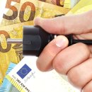 Männliche Hand hält Stromstecker vor Euro-Banknoten