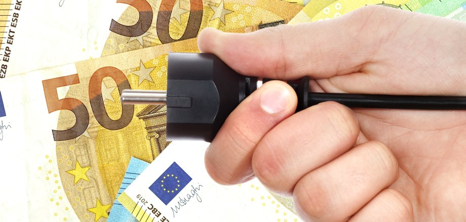 Männliche Hand hält Stromstecker vor Euro-Banknoten