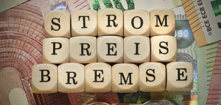 Das Wort "Strompreisbremse" in deutscher Sprache auf einem Stapel von Euro-Banknoten und -Münzen als HInweis auf die Folge der ständig steigenden Strompreise.