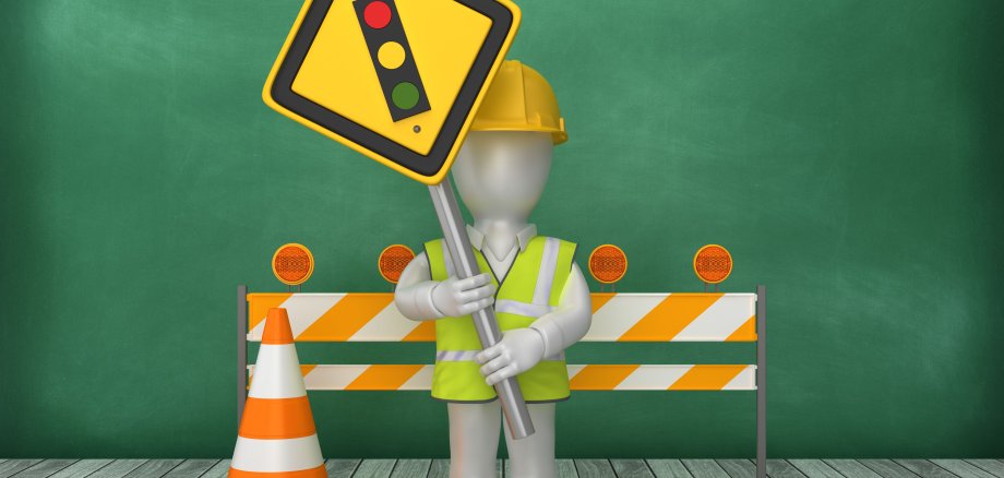 Auf dem Foto sieht man ein Legomännchen mit einem Schild in der Hand, auf dem eine Ampel abgebildet ist, hinter vor einer rot-weißen Straßensperre.