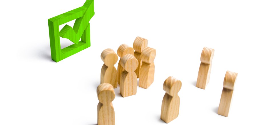 Kleine Holzmännchen bei einer Wahl, einer Abstimmung oder einem Referendum schauen auf ein grünes Häkchen in einer Box. 