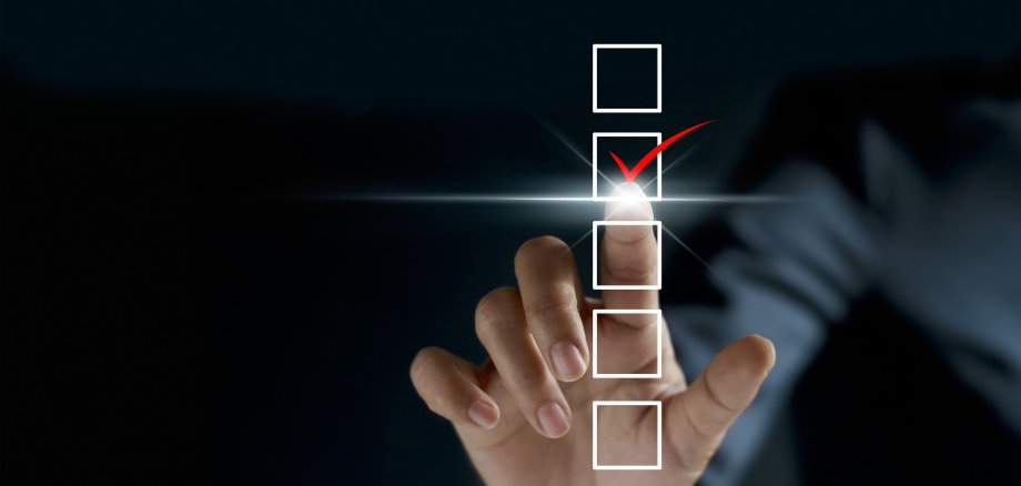 Schwarzgrundiges Bild mit 4 weißen Feldern. Der Zeigefinger einer Hand lässt im 2. Kästchen von oben einen roten Haken erscheinen