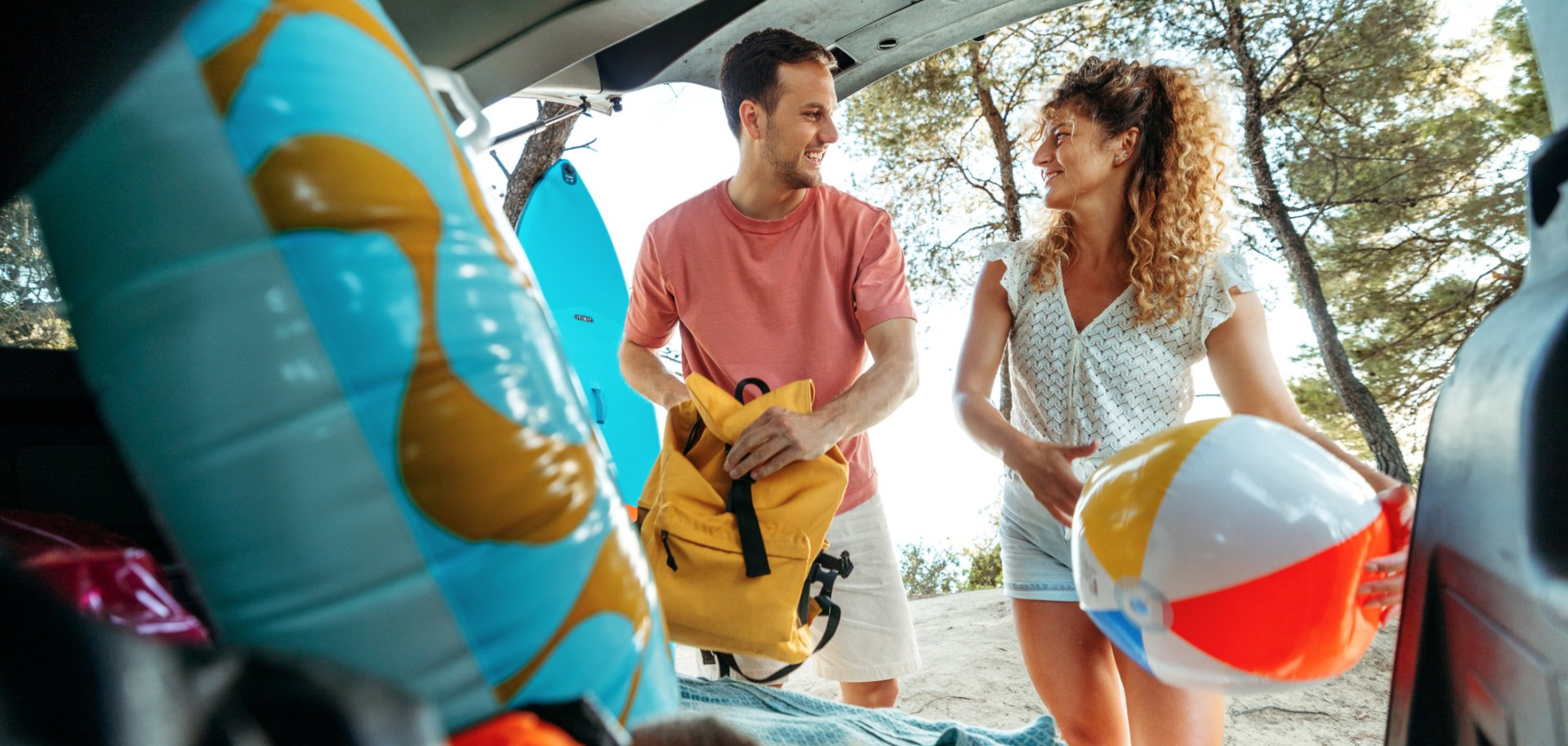 Young couple unpacking car trunk while getting ready for the beach adventure
