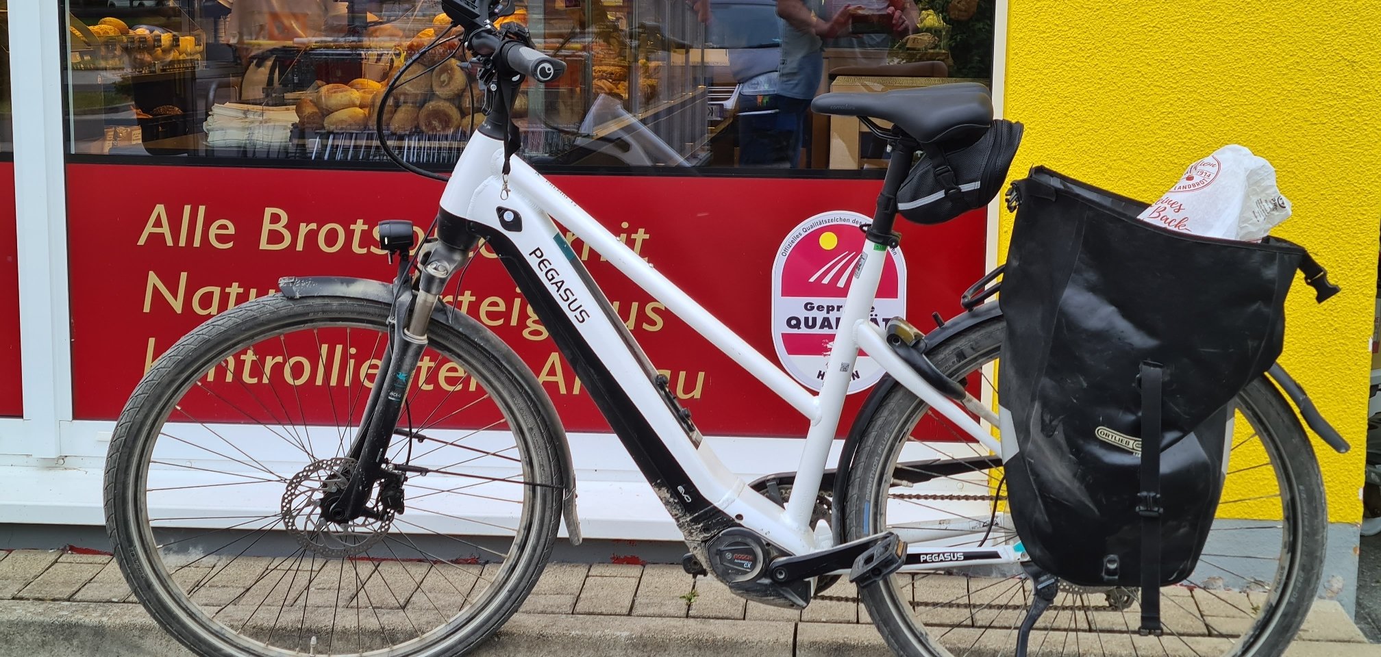 Weißes Pedelec vor dem Schaufenster einer Bäckerei.