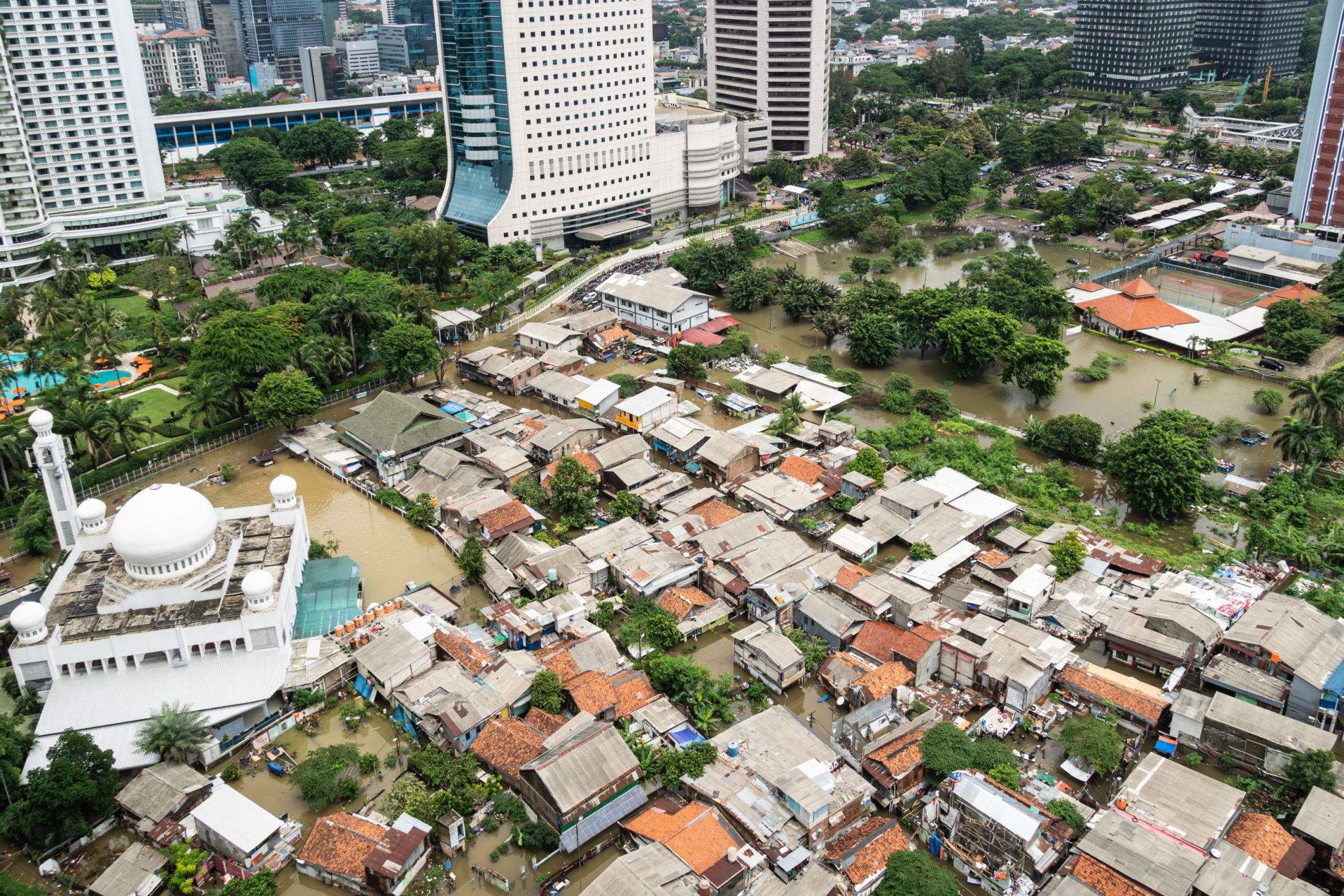 Die überflutete Straße in einem armen Wohnviertel im Herzen der  indonesischen Hauptstadt Jakarta, die die großen Ungleichheiten mit den  sie umgebenden modernen Hochhäusern verdeutlicht / The flooded street in a poor residential district in the heart of Jakarta city in Indonesia capital city which show huge inequalities with modern towers surrounding it
