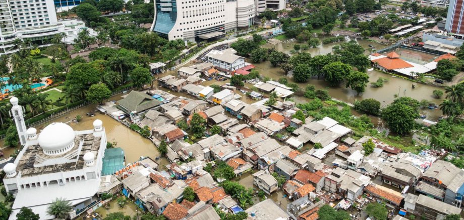 Die überflutete Straße in einem armen Wohnviertel im Herzen der  indonesischen Hauptstadt Jakarta, die die großen Ungleichheiten mit den  sie umgebenden modernen Hochhäusern verdeutlicht / The flooded street in a poor residential district in the heart of Jakarta city in Indonesia capital city which show huge inequalities with modern towers surrounding it